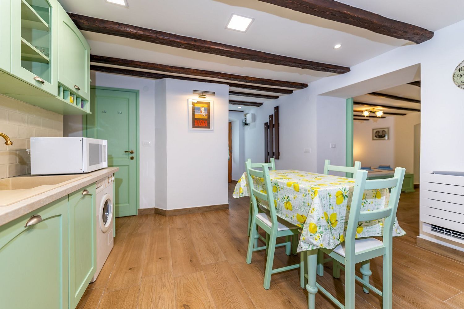 A kitchen with a dining area, wooden beams, a washing machine, and a microwave.