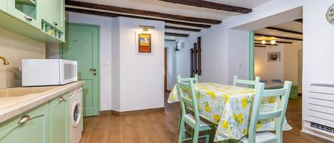 A kitchen with a dining area, wooden beams, a washing machine, and a microwave.