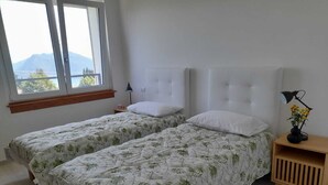 Makuuhuoneessa on kaksi erillistä sänkyä, yöpöytä, lamppu ja ikkuna, josta avautuu näkymä vuorille.