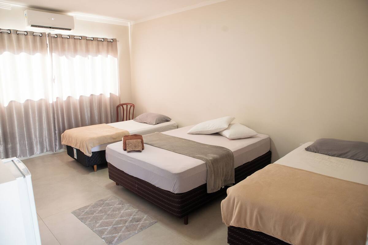 A hotel room with two beds, a small table, a chair, and a window with curtains.