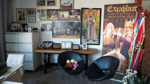 A room with a desk, two black chairs, a cabinet, and various framed pictures on the wall. - POUSADA CASTELO DO REI (Penha)