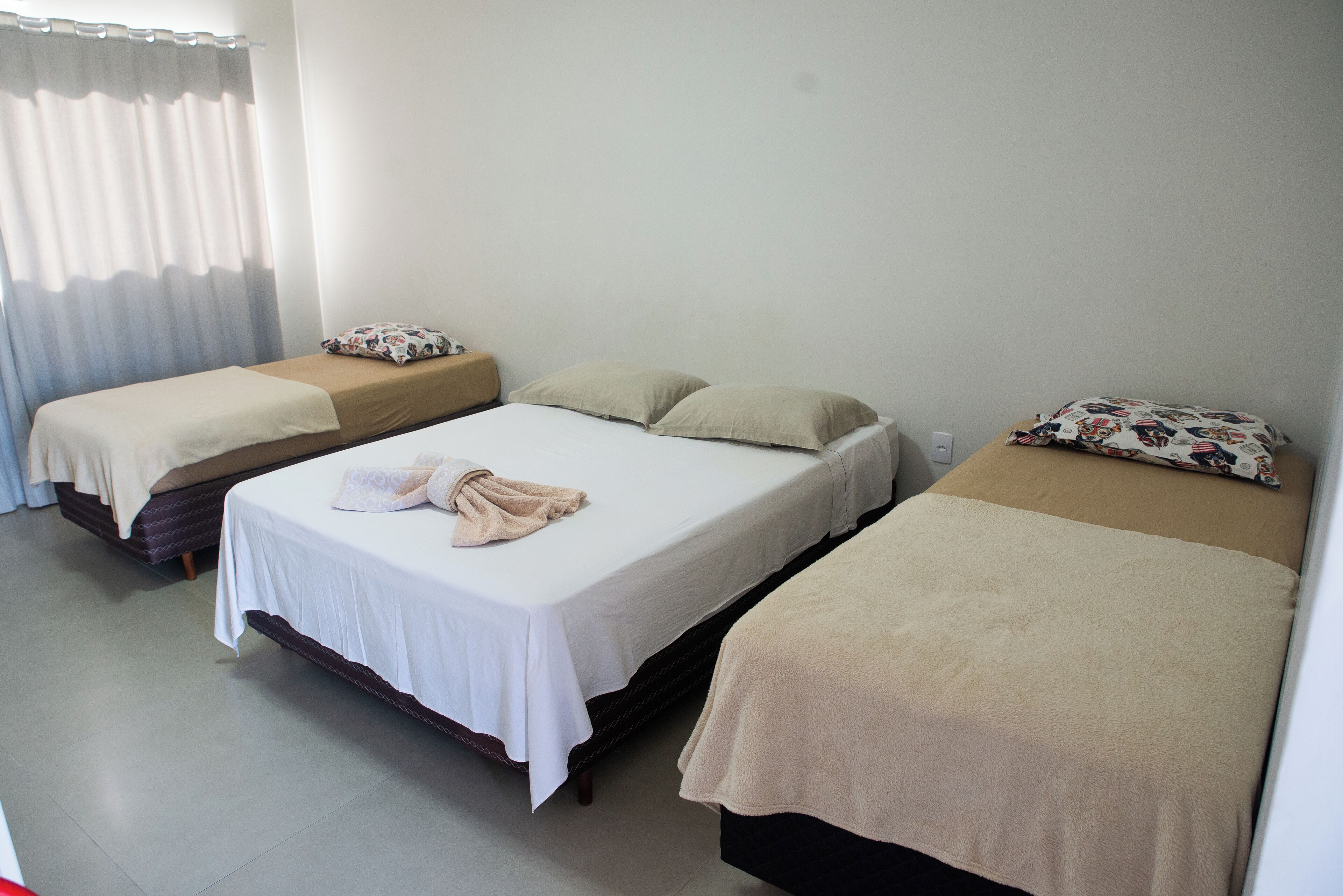 A hotel room with three beds, each with a different style of bedding and pillows.