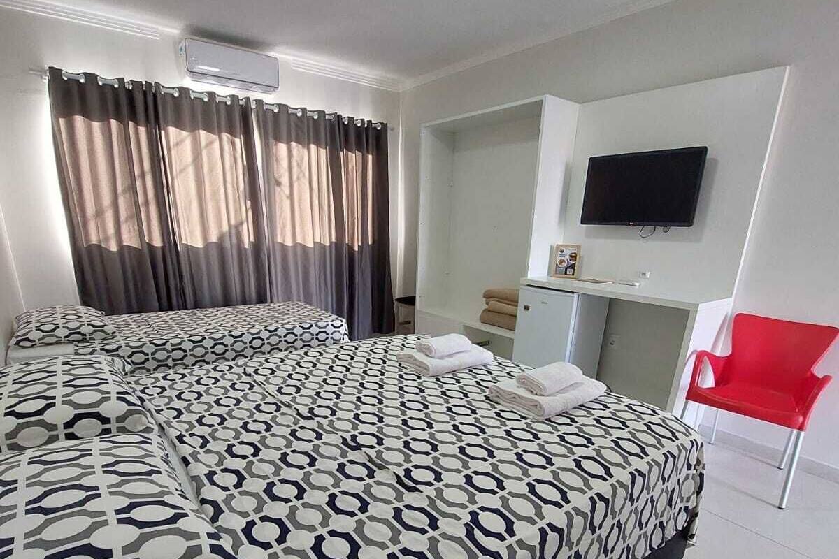 A hotel room with a large bed, a TV mounted on the wall, and a red chair.