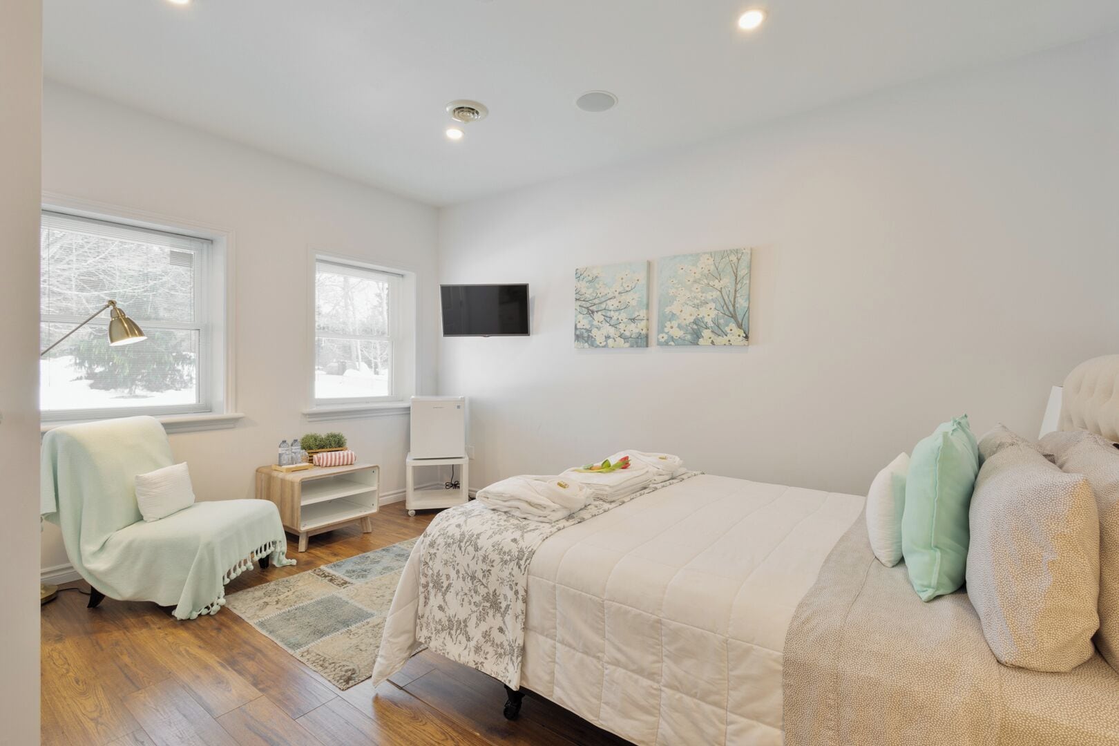 A bedroom with a bed, a chair, a desk, and artwork on the wall.