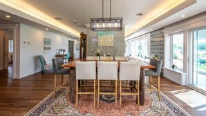A spacious dining area with a large wooden table, four chairs, and a modern chandelier. - Ocean Bay View Luxury Guesthouse (Musquodoboit Harbour)