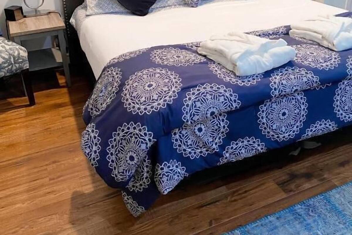 Ein ordentlich bezogenes Bett mit einem blau-weißen Muster, zwei schwarzen Kissen und einem dekorativen Wandbild darüber.
