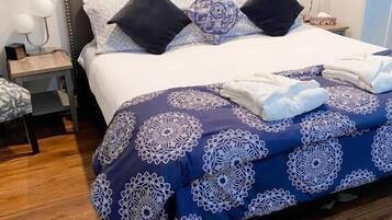 Una cama bien hecha con una colcha azul y blanca estampada, dos almohadas negras y un tapiz decorativo sobre la cama.