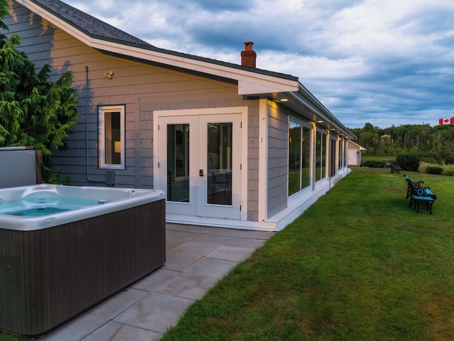 Ein modernes Haus mit Whirlpool, überdachter Terrasse und gepflegtem Rasen.