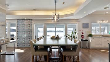 A spacious dining area with a long table, multiple chairs, and a view of a lake through large windows.