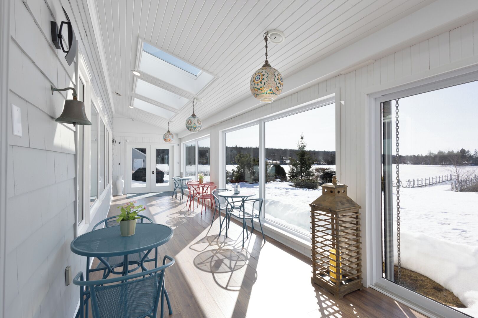 A sunlit room with large windows, a wooden ceiling, and a view of a snowy landscape.