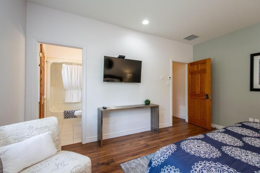A bedroom with a bed, a TV mounted on the wall, a console table, and a door leading to a bathroom.