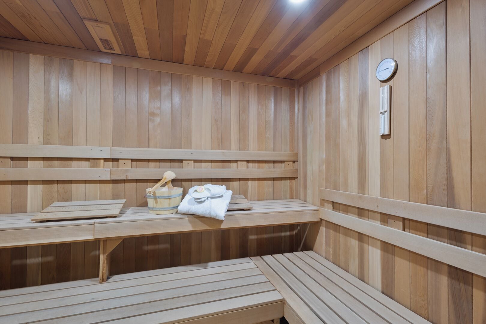 A sauna room with wooden benches and a bench seat, a wooden bucket, and a towel.