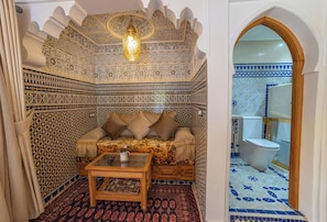 A room with a patterned wall, a sofa with cushions, a wooden coffee table, and a bathroom visible through an archway.