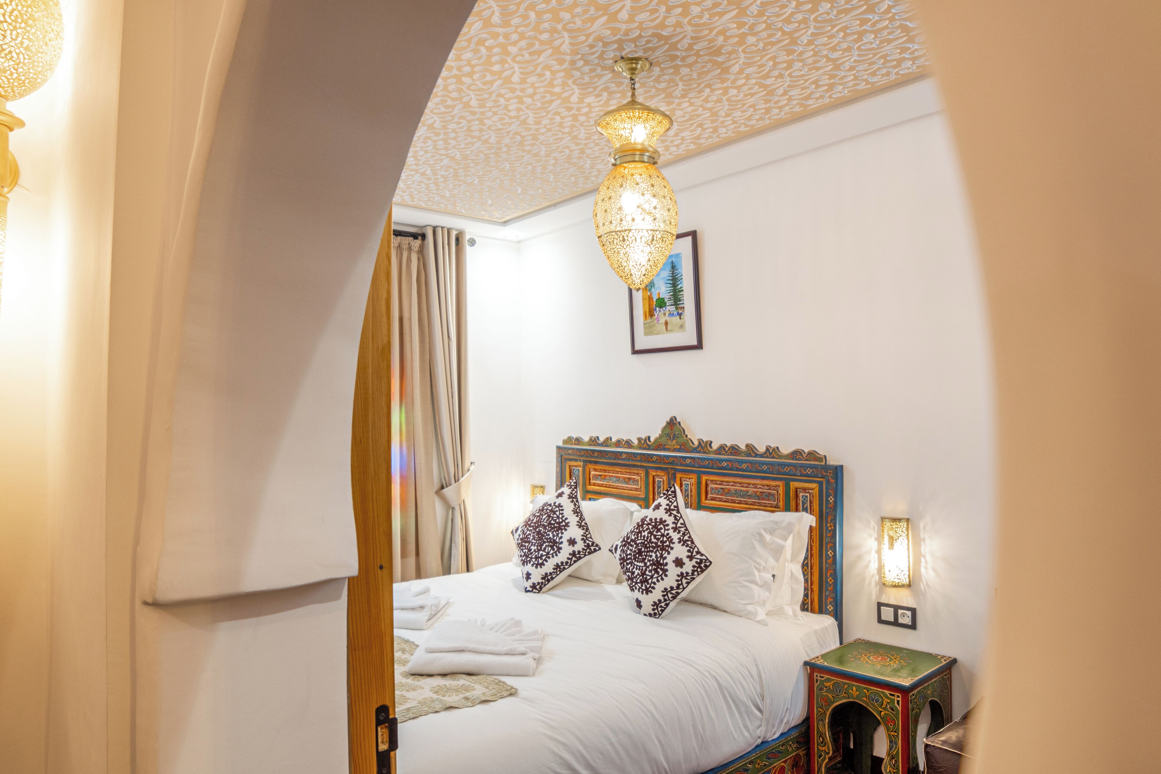 A hotel room with a large bed, a decorative ceiling, and a small table with a lamp.