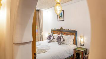 A hotel room with a large bed, a decorative ceiling, and a small table with a lamp.