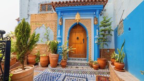 Ein traditionelles marokkanisches Haus mit blauer Fassade, einer Holztür und Terrakottatöpfen mit Pflanzen.