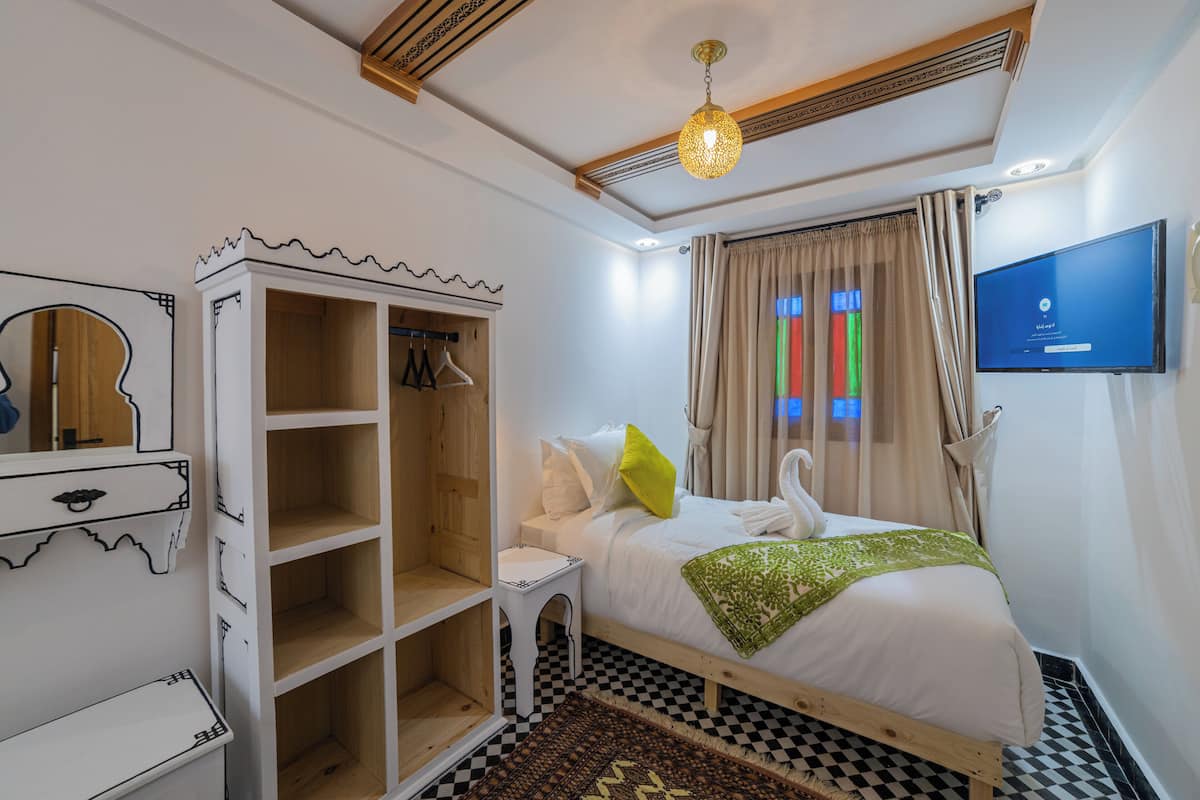 A bedroom with a bed, a wardrobe, a small table, a TV, and a window with curtains.