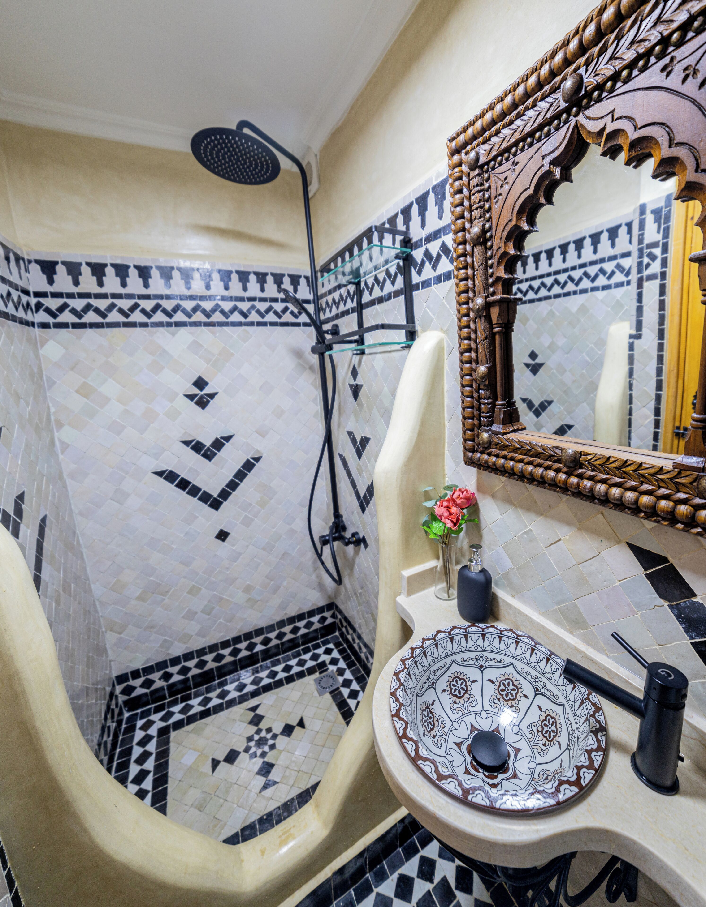 Un baño con ducha, un lavabo con una pileta decorativa y un espejo con un marco ornamentado.