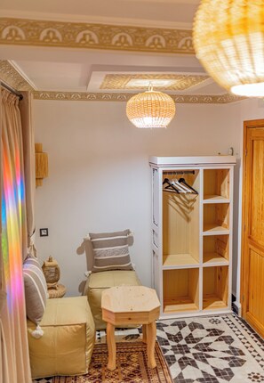 A room with a white wardrobe, a small table, a hanging light fixture, and a patterned floor.