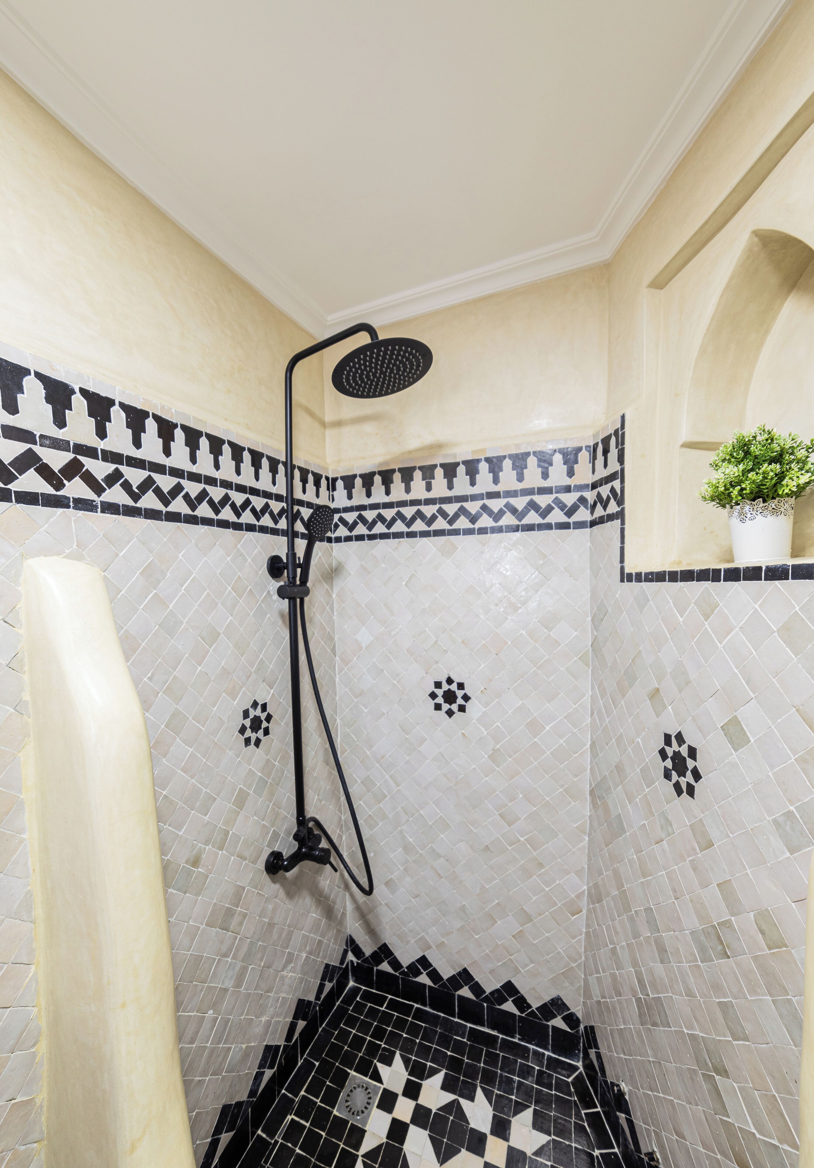 Een douche met een zwarte handdouche, een witte handdoek en een potplant op een plank.