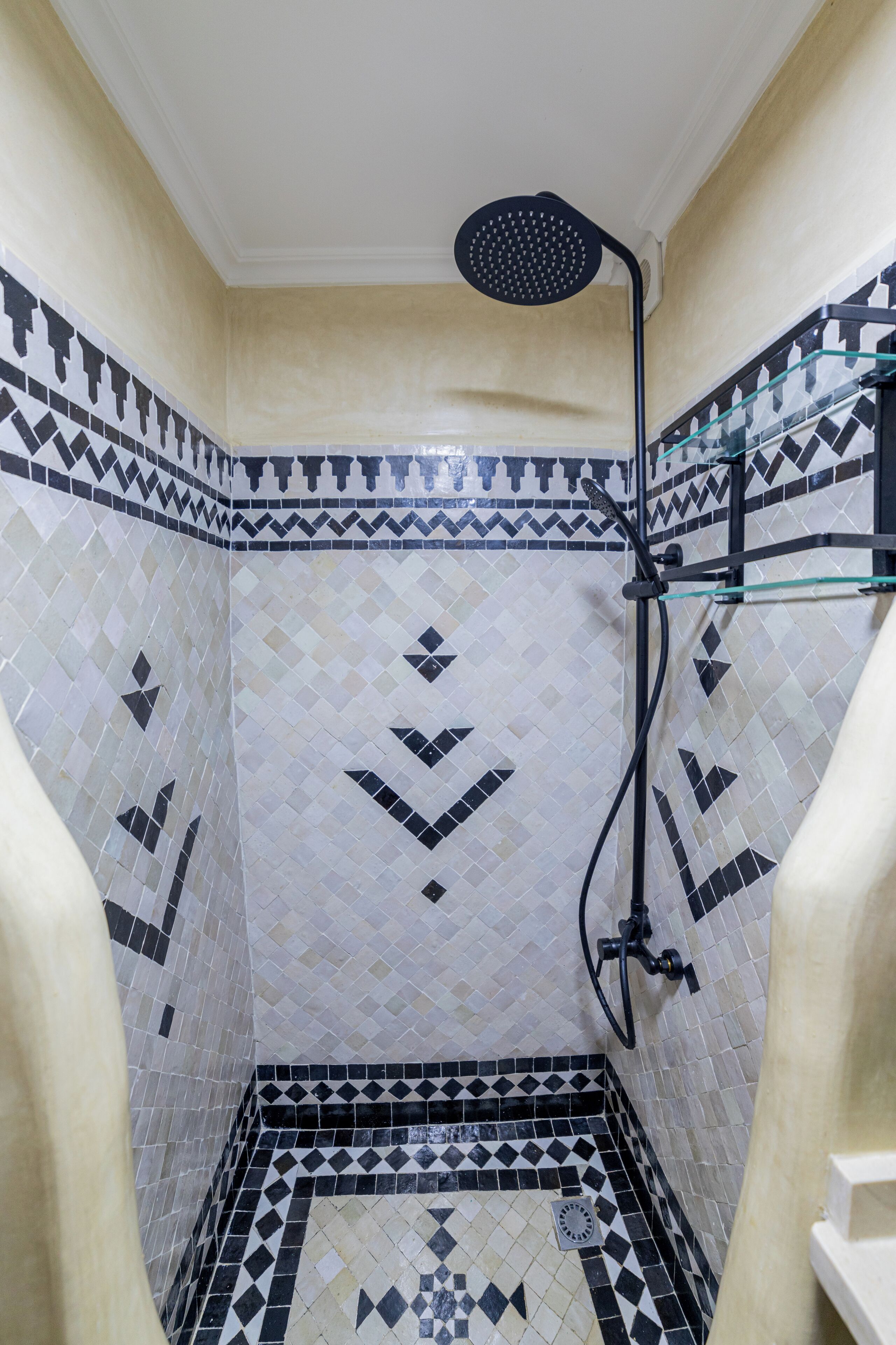 A small, tiled shower area with a showerhead and a glass shelf.