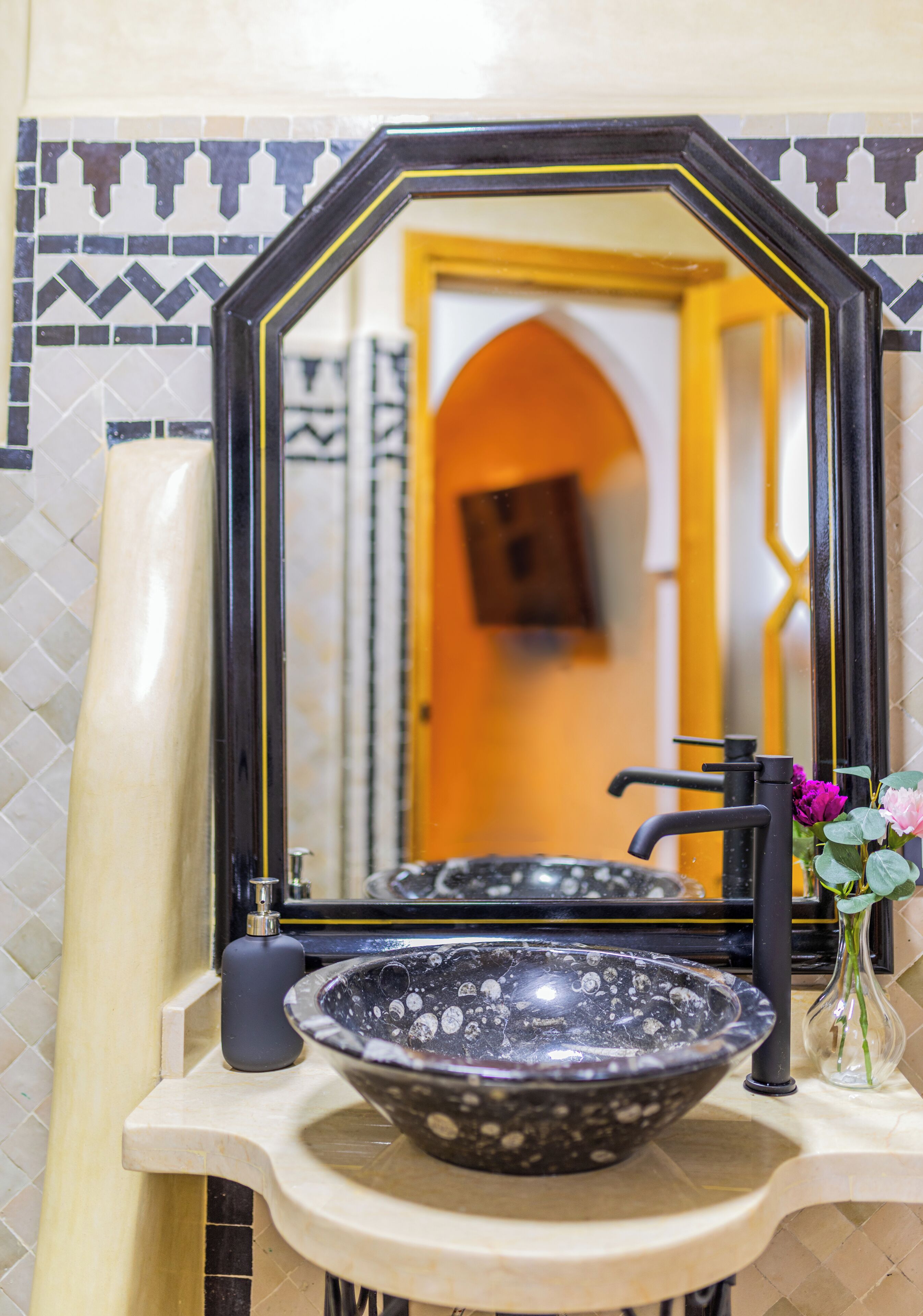 A bathroom with a black and white patterned bowl sink, a black faucet, and a mirror with a black frame.