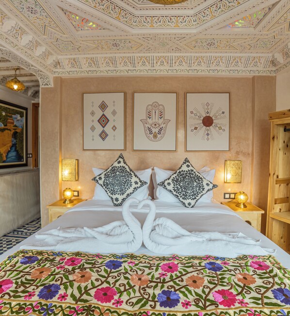 A hotel room with a bed, two nightstands, a wall with three framed artworks, and a decorative ceiling. - Dar MD (Chefchaouen)
