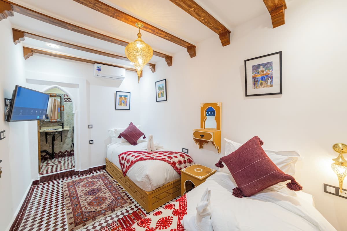 A bedroom with a bed, a wooden headboard, a red and white patterned rug, a hanging light fixture, and a wall-mounted mirror.