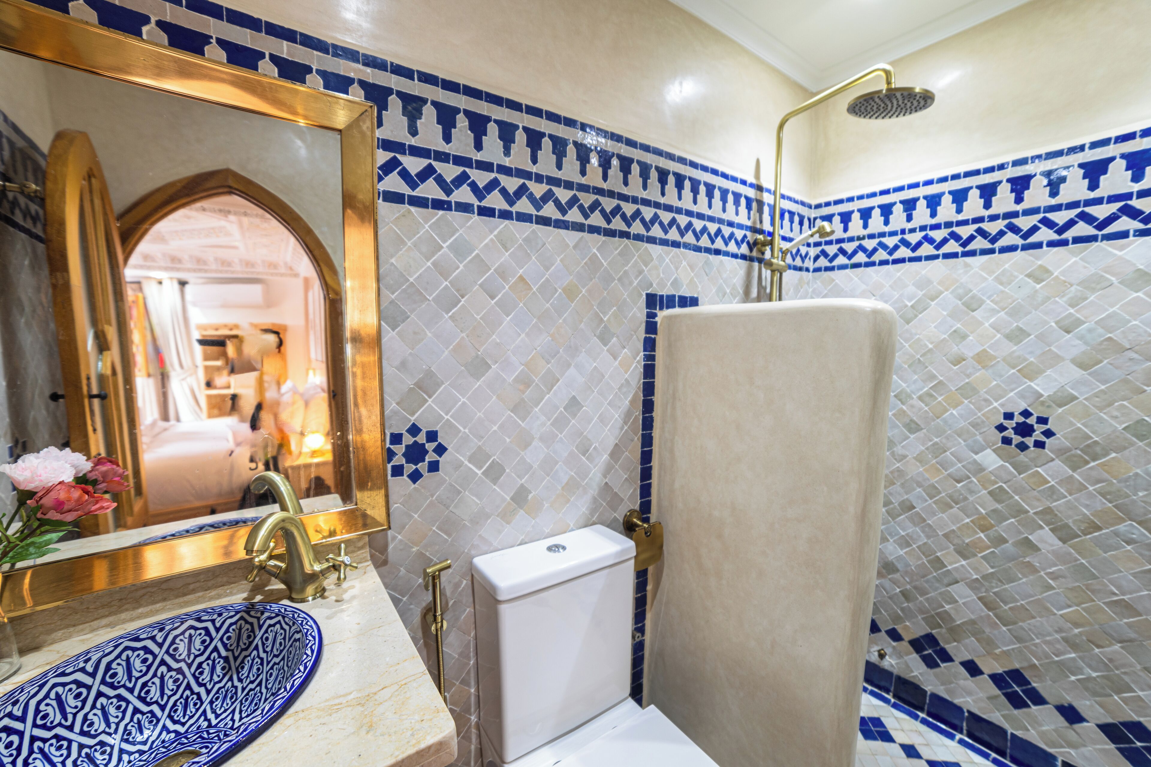 A bathroom with a white sink, blue patterned basin, and a shower with a gold faucet.