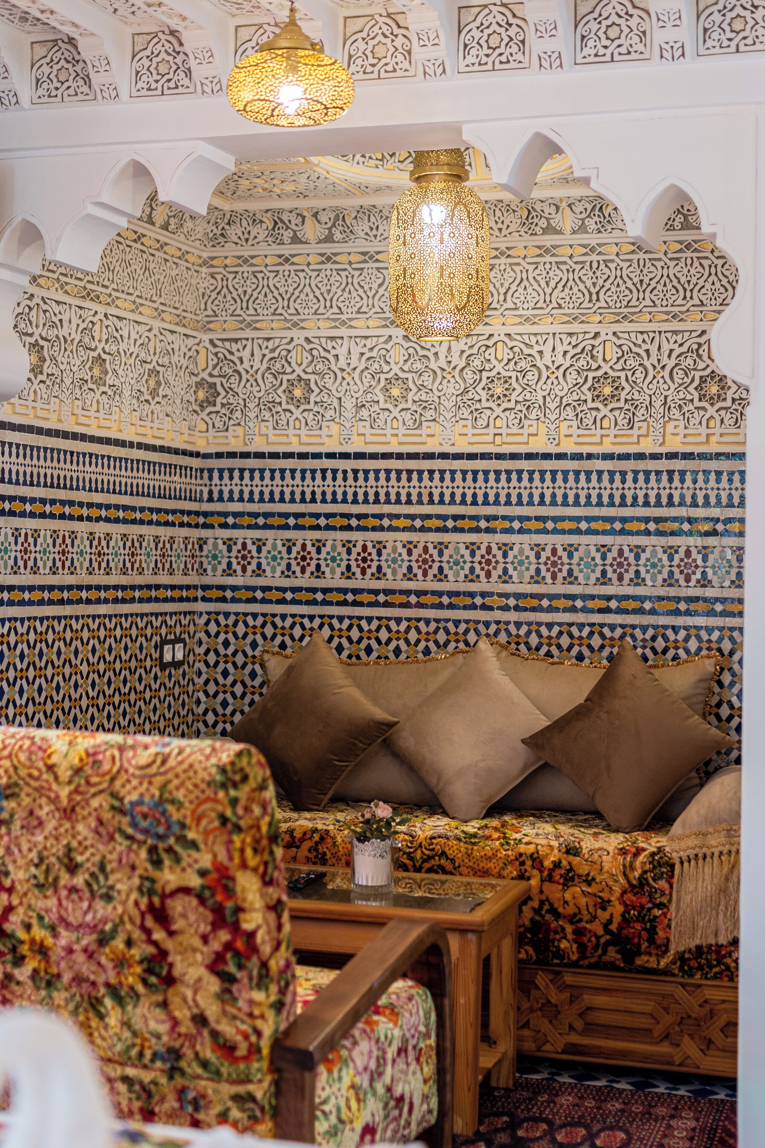 A room with a patterned wall, a sofa with cushions, a chair, and a hanging light fixture.