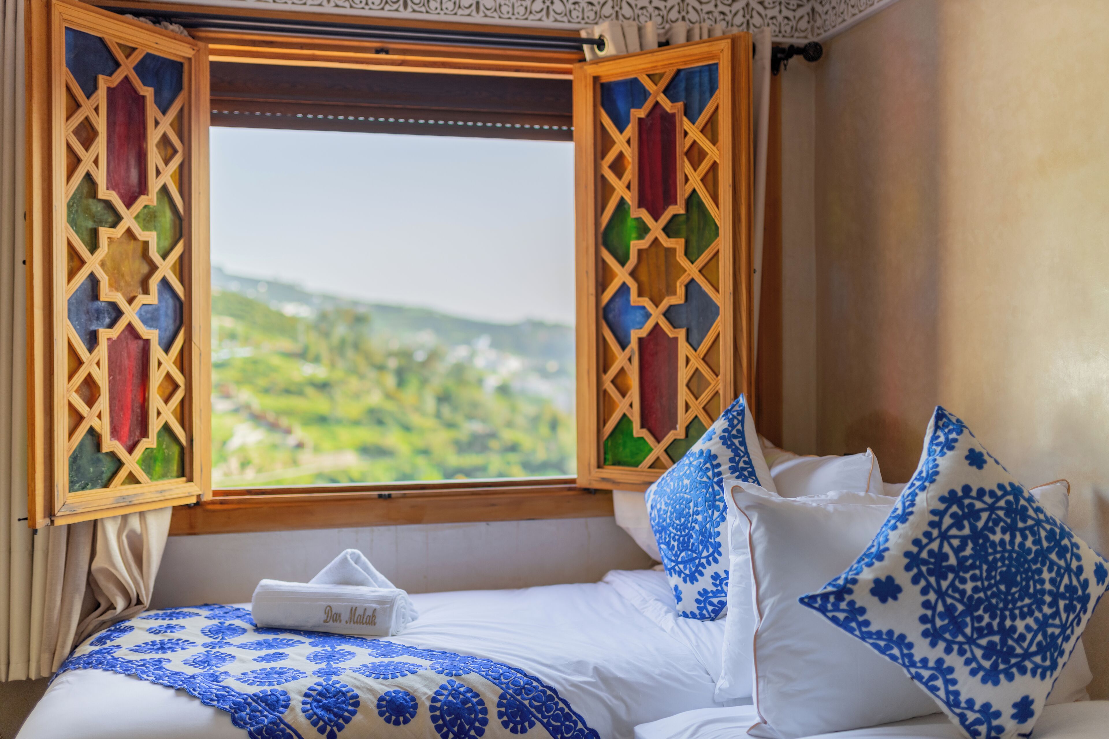 Una cama con vista a un paisaje verde a través de una ventana con un diseño de celosía de madera.