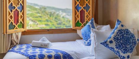 Una cama con vista a un paisaje verde a través de una ventana con un diseño de celosía de madera.