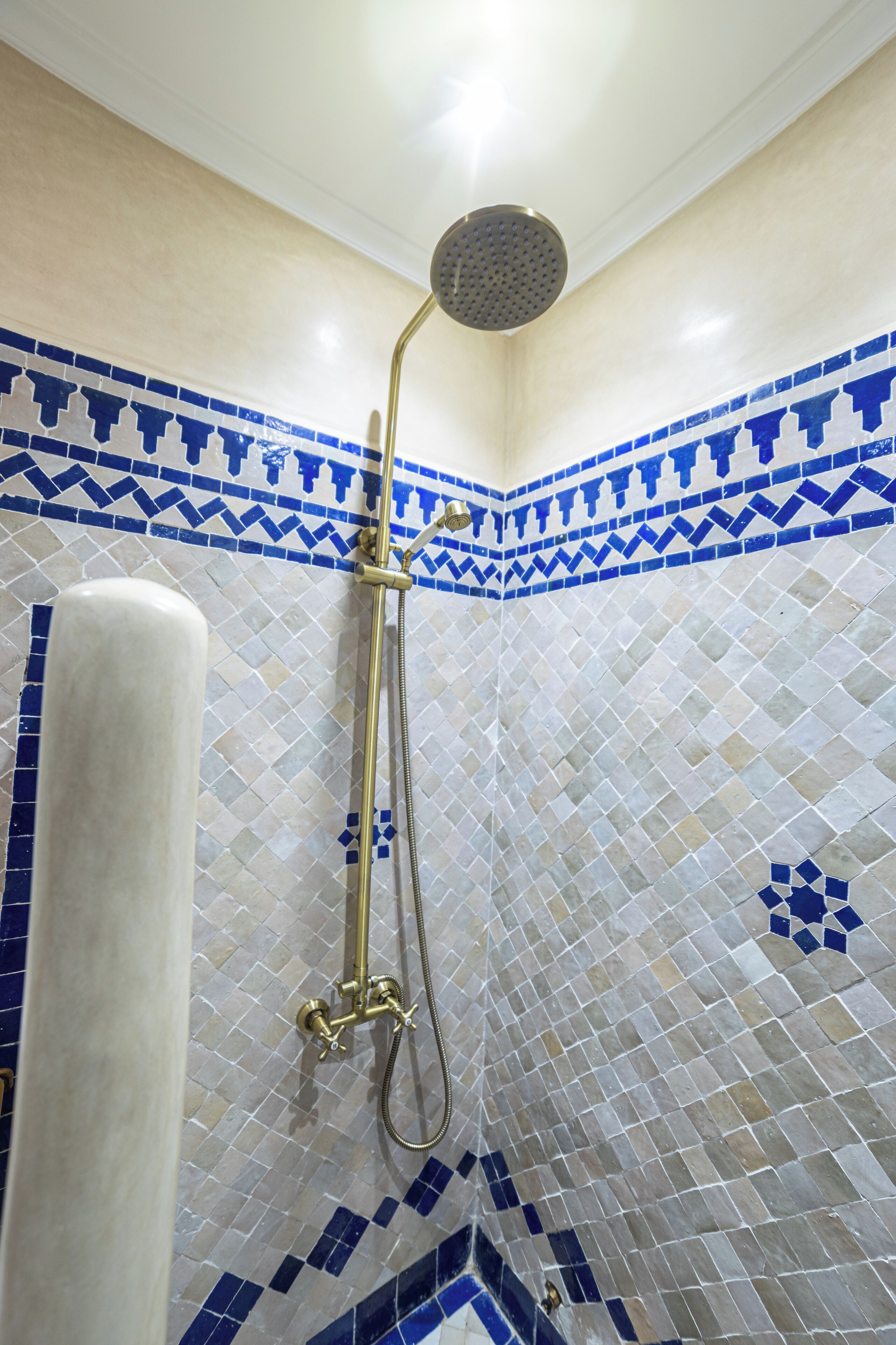 A shower with a gold showerhead and a white column.