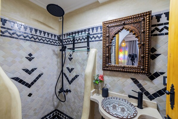 Un baño con ducha, lavamanos y espejo con un marco ornamentado.