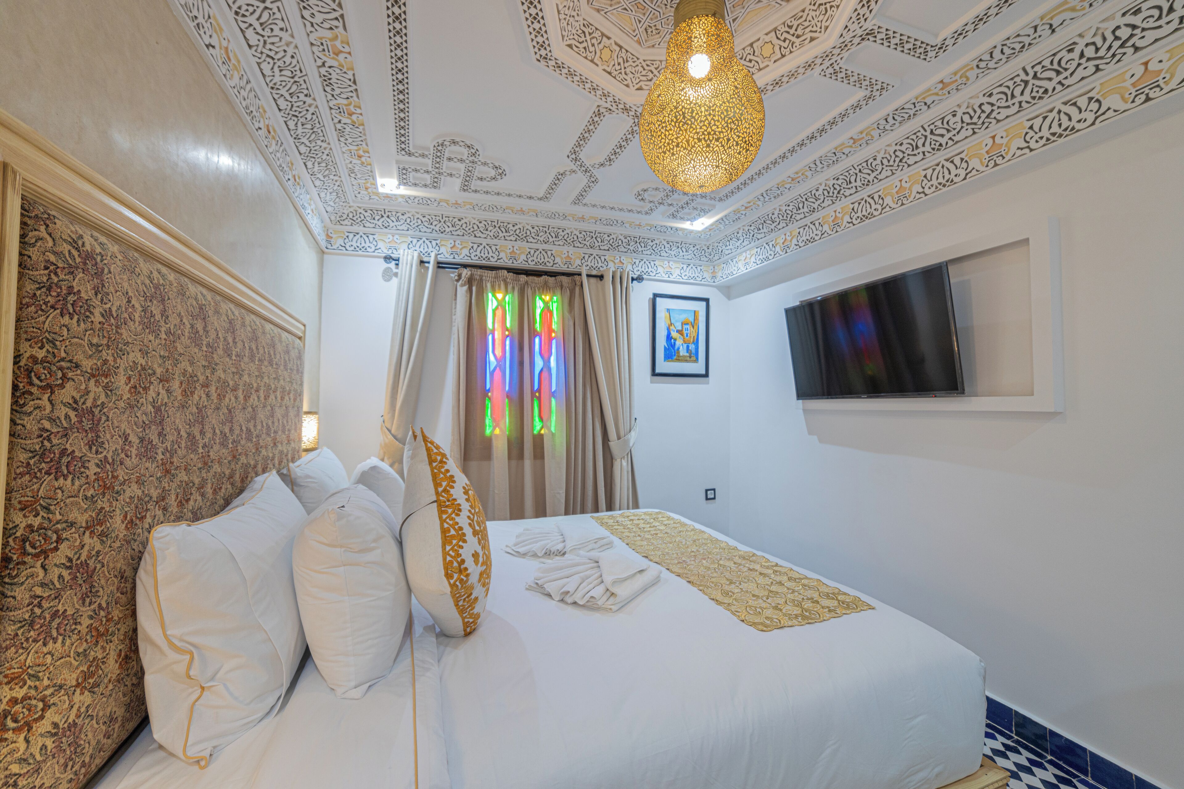 Quarto de hotel com cama, cortinas, televisão e teto estampado.