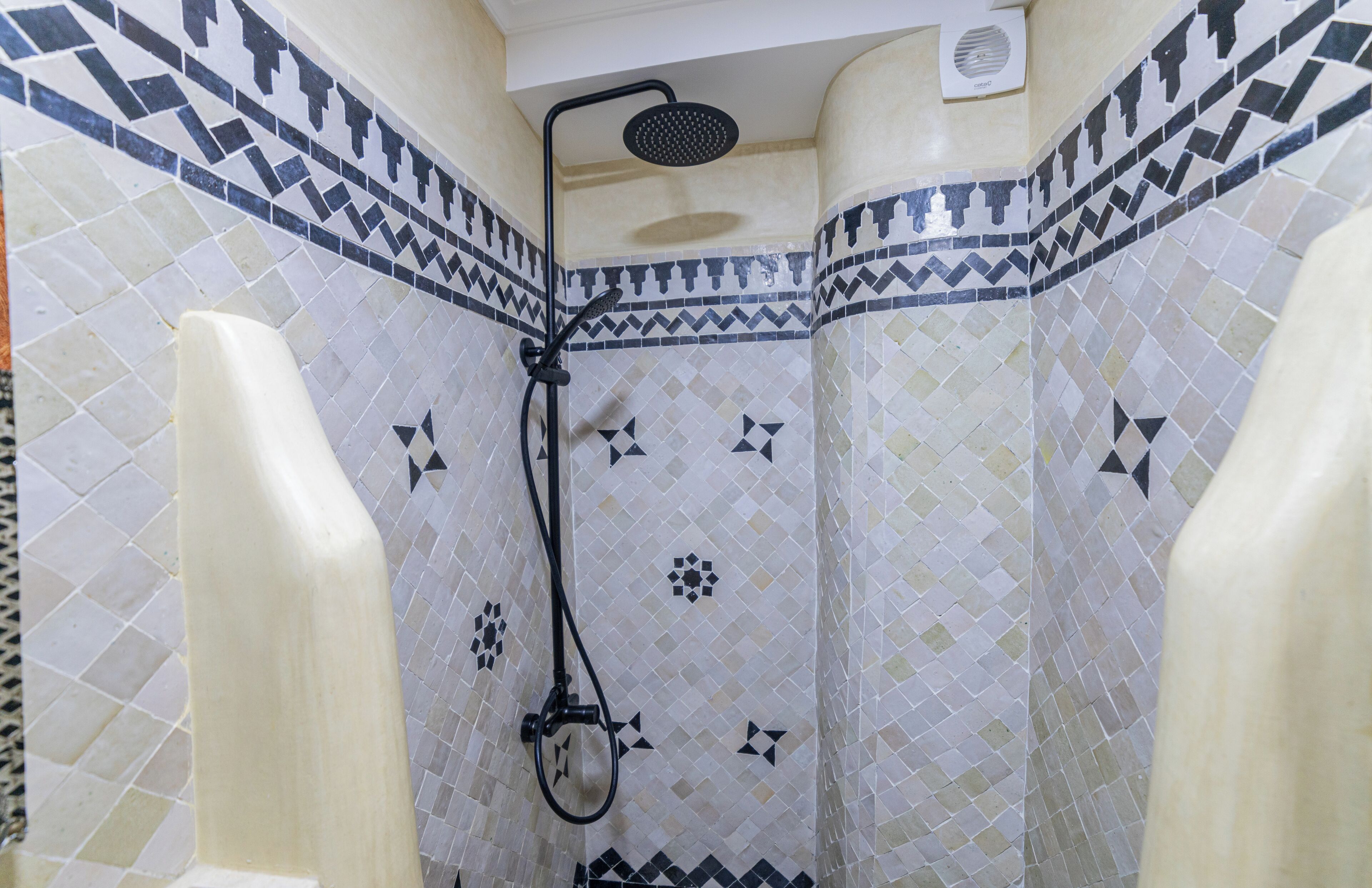A shower with a black hose and a handheld showerhead, surrounded by patterned tiles.