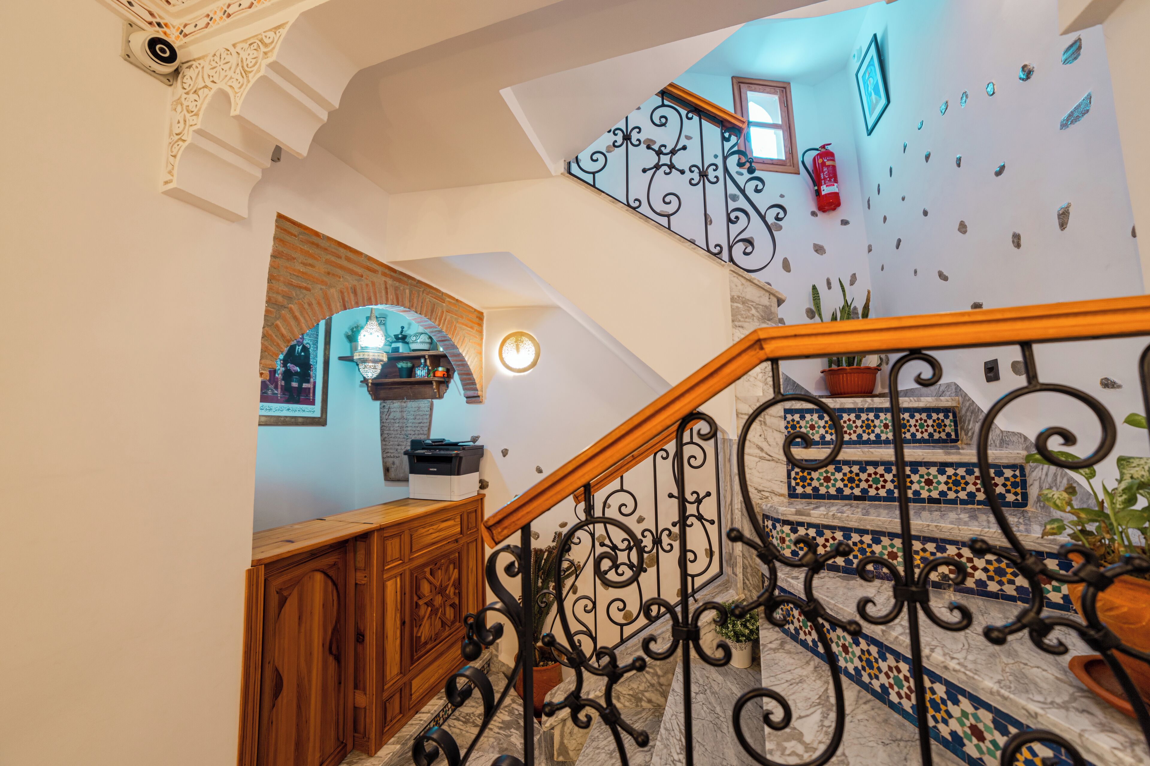 A staircase with ornate black railings, a wooden handrail, and a tiled floor with a geometric pattern.