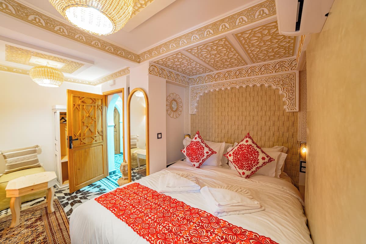 A hotel room with a large bed, a wooden door, a small table, and a patterned rug.