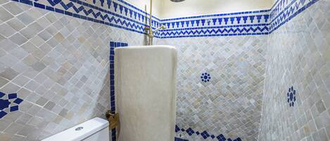 Baño con ducha, inodoro y lavamanos, con azulejos de mosaico azul y blanco.