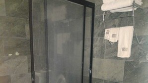 A bathroom with a glass shower enclosure, a toilet, and a towel rack with folded towels. - Hotel Centro Valles  (Ciudad Valles)