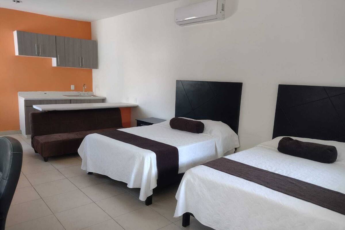 A hotel room with two beds, a sofa, a small desk, and a kitchenette.