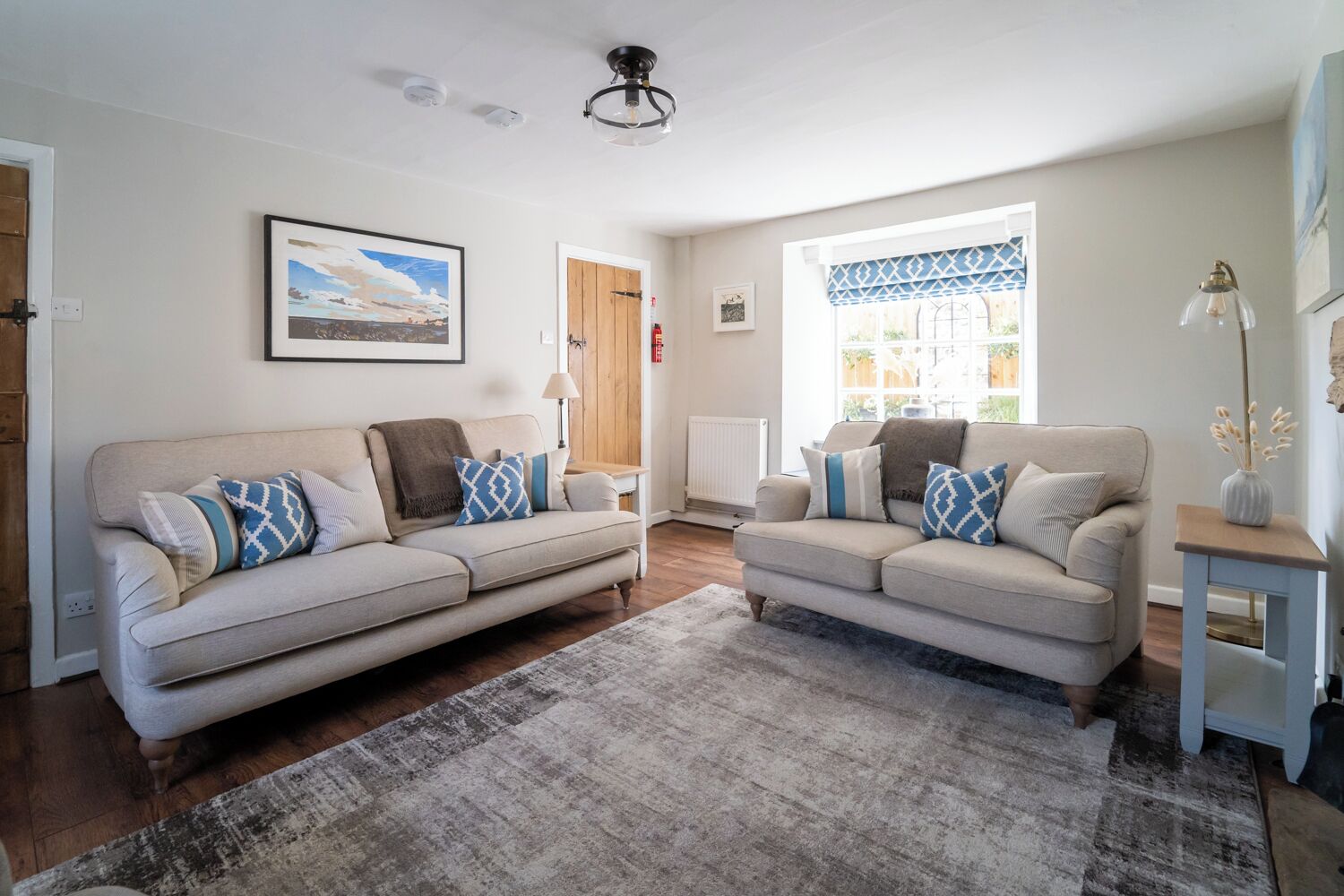 A living room with two beige sofas, a patterned rug, and a ceiling light fixture.