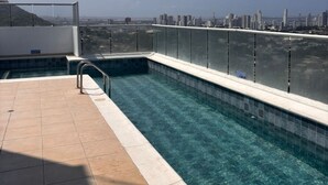 Une piscine sur le toit avec une eau d’un bleu limpide, une terrasse carrelée et une vue sur le paysage urbain en arrière-plan.