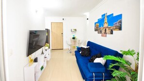 Un salon moderne avec un canapé bleu, un téléviseur à écran plat et une petite table agrémentée d’objets décoratifs.