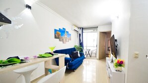 Un salon moderne avec un canapé bleu, une table à manger et des chaises, un téléviseur et une petite plante.