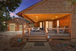 Una cabaña de madera con un porche cubierto, un garaje y un patio con mobiliario exterior.