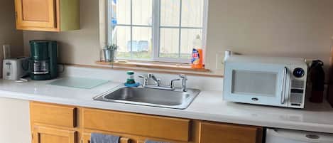 A compact kitchen with a sink, a microwave, and a refrigerator. There's a window with a checkered curtain, and a 'No Smoking' sign on the wall.