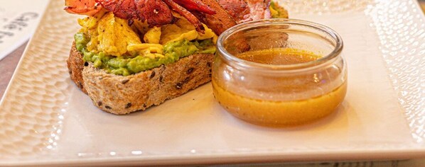 Un sandwich à l’avocat et au bacon, servi sur une tranche de pain, accompagné d’un petit pot de sauce.