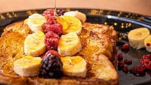 A plate of French toast topped with sliced bananas, berries, and syrup. - NEIZAN HOTEL (Antigua Guatemala)