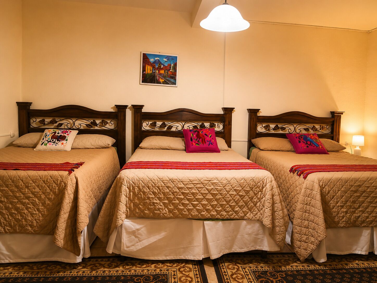 Habitación de hotel con tres camas, cada una con cabecero de madera, ropa de cama color beige y almohadas decorativas. Un cuadro cuelga en la pared sobre las camas.